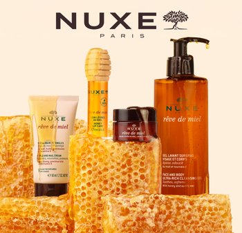 NUXE Rêve de Miel skincare products arranged with honeycomb. Features various packaging shapes: a pump bottle, jar, tube, and stick.