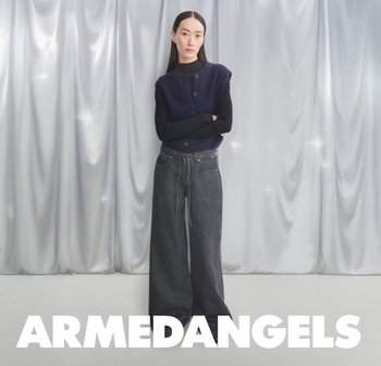 Navy knitted sleeveless top with front buttons paired with loose-fitting, dark gray high-waisted jeans, set against silver draped fabric backdrop.