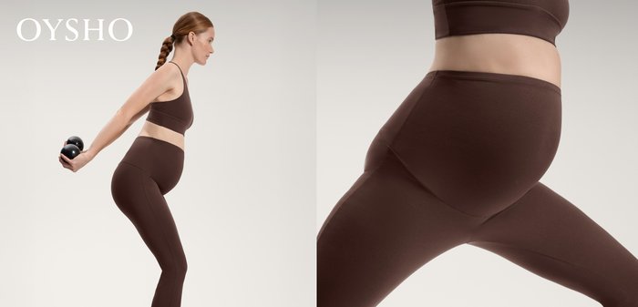 Schwangere Frau in brauner Sportkleidung trainiert mit kleinen schwarzen Gewichten und streckt die Arme hinter sich gegen einen schlichten hellen Hintergrund aus.