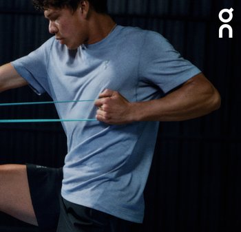 T-shirt de sport bleu clair en matériau doux, associé à un short noir. La personne utilise des bandes de résistance dans un cadre d'entraînement.