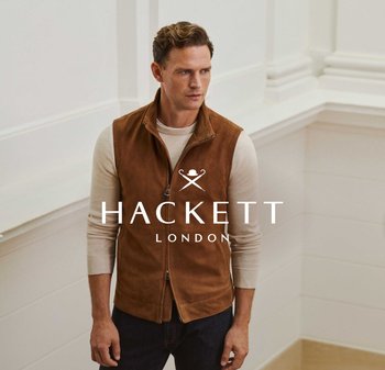 Homme portant un gilet zippé en daim marron par-dessus une chemise beige à manches longues, debout contre un mur blanc à panneaux à l'intérieur.