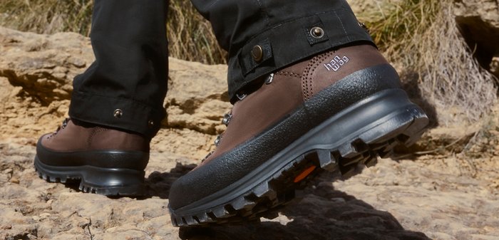 Bruine wandelschoenen met dikke zwarte zolen, gedragen door een persoon die op rotsachtig terrein buiten loopt.