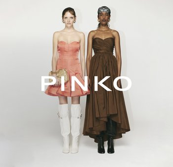 Two models stand side by side. The left wears a coral strapless dress and white knee-high boots. The right wears a brown strapless gown with draping.