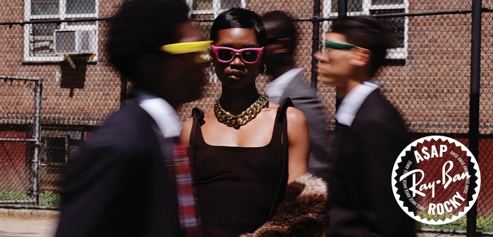 Grupa pięciu mężczyzn w garniturach, noszących różne okulary przeciwsłoneczne: w czerwonych, różowych, czarnych i niebieskich oprawkach. Istotne tekstury obejmują tkaniny garniturów i detale okularów.