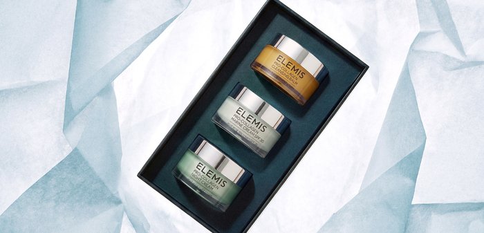 Trois pots de soins de la peau Elemis — baume nettoyant pro-collagène, crème marine SPF 30 et crème de nuit — disposés dans une boîte noire sur un tissu blanc.