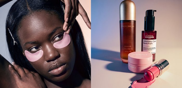 Femme à la peau foncée applique des patchs roses pour les yeux, à côté de quatre produits de soin, dont des sérums, une crème et un baume à lèvres, sur une surface claire.