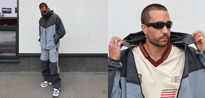 Ensemble de sport pour homme comportant un coupe-vent gris et noir avec capuche et poches, associé à un pantalon assorti et des chaussures blanches.