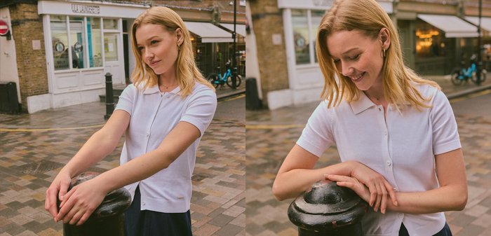 Joven mujer con camisa blanca de manga corta sonriendo y apoyada en un bolardo negro en una calle adoquinada en un entorno urbano.