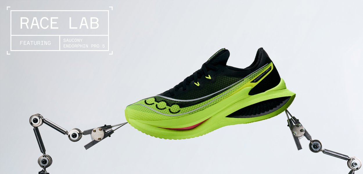 Chaussure de course Saucony Endorphin Pro 5 vert vif et noir tenue par deux bras robotiques sur un fond gris uni.