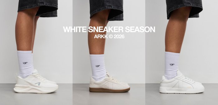 Ben iført hvide crew sokker og sorte shorts, med to stilarter af hvide sneakers med tykke såler på en grå gulv.