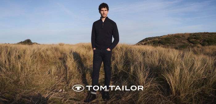 Granatowy sweter zapinany na zamek, ciemne dżinsy i czarne buty. Noszone na trawiastym terenie pod bezchmurnym niebem. Logo marki na dole na środku.