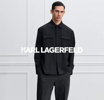 Black button-up shirt with two chest pockets, made of smooth fabric, paired with grey trousers. Simple, structured design without patterns.