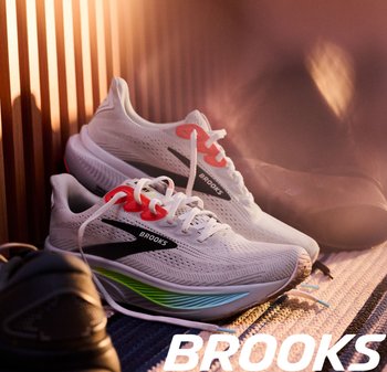 Witte hardloopschoenen van mesh materiaal hebben feloranje veters, zwarte accenten aan de zijkant en een groen-blauw verlopen op de zool.