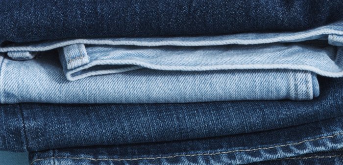Pile de jeans en denim pliés dans différentes nuances de bleu, montrant la texture du tissu et les détails des coutures.