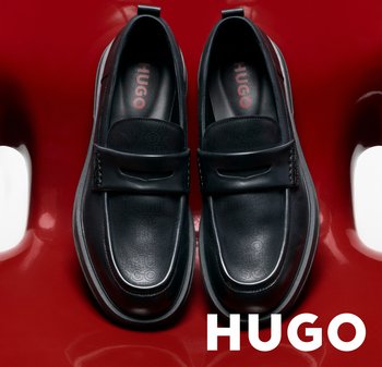 Mocasines de cuero negro con un diseño elegante sobre una silla roja de alto brillo, con la marca "HUGO" dentro y debajo de los zapatos.