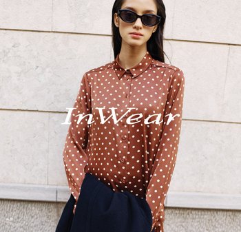 Braune Bluse mit langen Ärmeln, großen weißen Punkten, durchgehender Knopfleiste und Kragen, kombiniert mit einer dunkelblauen Außenschicht.