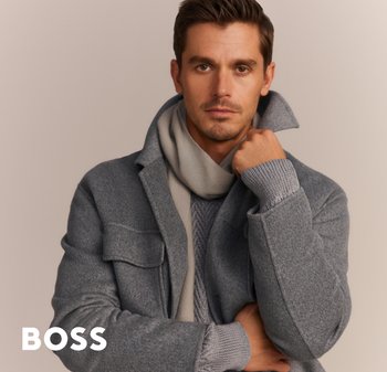 Cappotto grigio in lana con colletto alto, indossato sopra un maglione grigio a trama. Una sciarpa grigia chiara completa l'outfit. Design pulito e moderno.