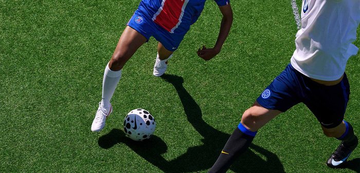 Kaks jalgpallurit võistlevad mustvalge palliga rohelisel murul, kandes sinist ja valget spordiriietust ning krampe.