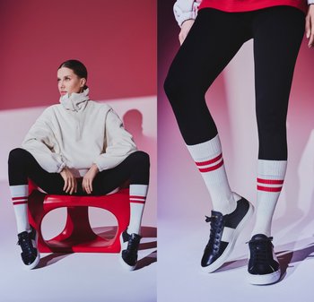 Weißer Pullover mit hohem Kragen, schwarze Leggings und kniehohe weiße Socken mit roten Streifen. Schwarze Sneakers mit weißen Akzenten. Roter Hocker.