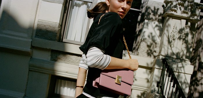 Gonna nera svasata, top a maniche lunghe bianco a strisce stratificato, mentre porta una borsa a tracolla rosa testurizzata con una catena dorata e una chiusura geometrica.