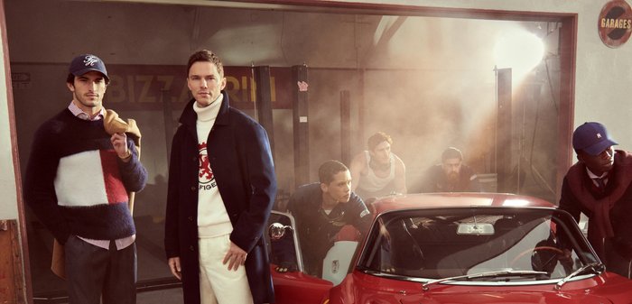 Gruppe von sechs Personen in einer Garage mit einem roten Auto. Vielfältige Kleidung wie Pullover, Mäntel und eine Mütze. Reichhaltige Texturen und Farben.