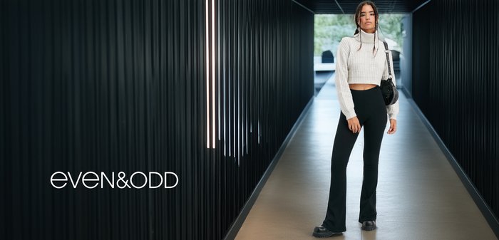 Zwarte wijde broeken, geribbelde witte cropped sweater en zwarte schoudertas. Gladde, gestructureerde materialen benadrukt in een moderne gang.