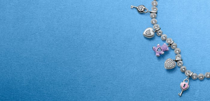 Silver charm bracelet with clear gems, featuring heart, key, and purple bear-shaped charms on a blue textured background.