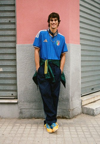 Niebieska koszulka piłkarska z Włoch z białymi akcentami, luźne granatowe spodnie i kolorowe trampki. Uzupełniona zielono-żółtą związana kurtką.