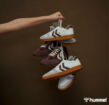 Witte en bordeauxrode sneakers met rubberen zolen, voorzien van een visgraatontwerp en contrasterende strepen, die aan veters van een arm hangen.