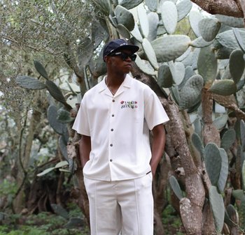 Kortermet skjorte med knapper i off-white med fargerik brodert tekst. Kombinert med matchende off-white bukser blant kaktuser.