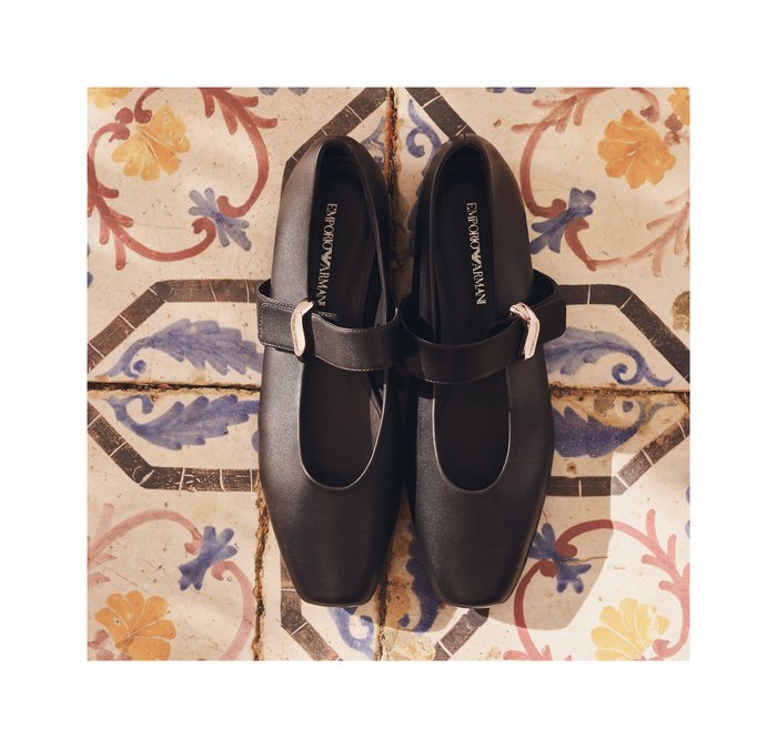 Coppia di scarpe nere Emporio Armani Mary Jane con fibbie argento appoggiate su un pavimento decorativo a motivi floreali.