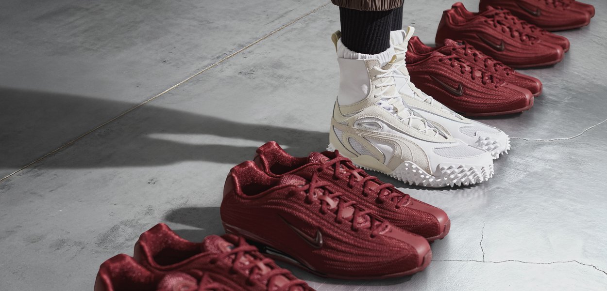 Dwa style obuwia: biały sneaker typu high-top z fakturowanymi akcentami oraz kilka czerwonych sneakerów typu low-top o gładkim wykończeniu, ułożonych na szarej powierzchni.