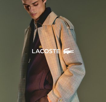 Abrigo de cuadros en tonos beige y azul, con cierre de botones al frente y un estilo casual en capas con un suéter azul marino debajo. Logotipo de LACOSTE visible.