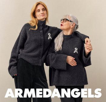 Zwei Frauen, eine jüngere und eine ältere mit grauen Haaren und Brille, tragen passende dunkelgraue Pullover mit einem weißen Schlüssel-Logo und stehen nah beieinander.