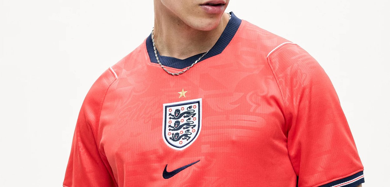 Jeune personne portant un maillot de football rouge de l'Angleterre avec le logo Nike et le blason de l'équipe visibles, sur un fond blanc uni.