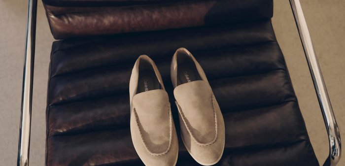 Chaussures beige en daim à enfiler placées côte à côte sur une chaise en cuir marron foncé avec des accoudoirs en métal.