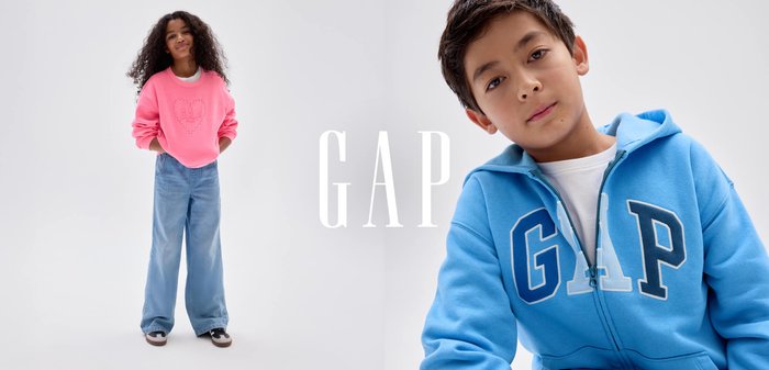 Junge steht mit den Händen in den Taschen und trägt einen blauen GAP-Hoodie, ein weißes T-Shirt, lockere Jeans und schwarze Turnschuhe vor einem schlichten grauen Hintergrund.