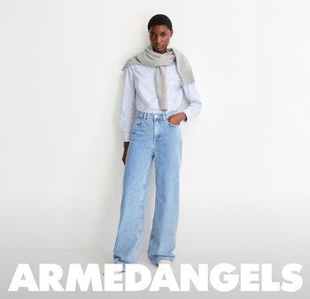 Helle blaue weit geschnittene Denim-Jeans mit hoher Taille, kombiniert mit einem weißen Hemd und einem grauen Pullover, der lässig über die Schultern gelegt ist.