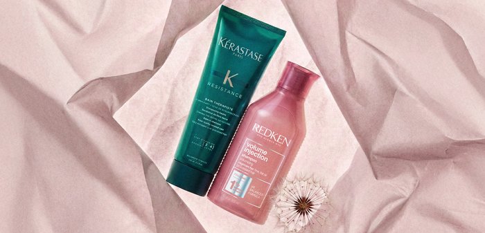 Bouteilles de shampooing Kerastase Resistance Bain Therapiste et Redken Volume Injection sur un tissu rose doux avec un pissenlit en graines.