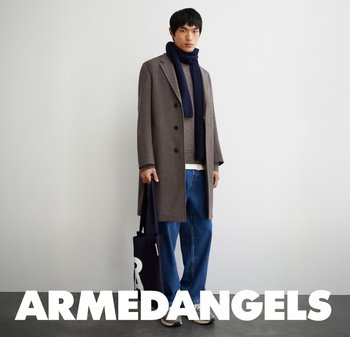 Brauner Wollmantel mit Doppelreiher-Design, getragen über einem leichten Pullover, kombiniert mit lockeren blauen Jeans und einem marineblauen Schal.