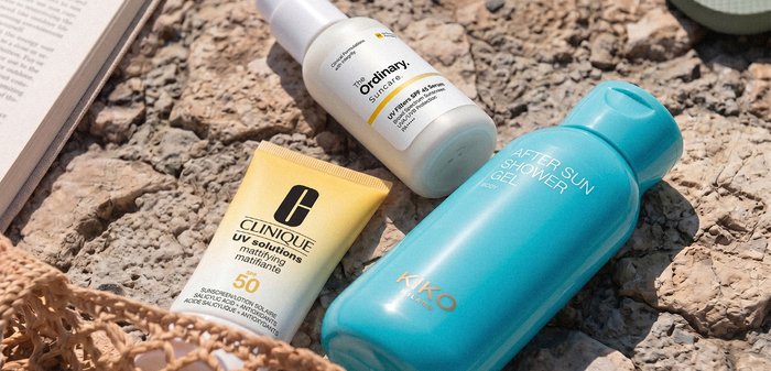 Crème solaire Clinique SPF 50, spray solaire The Ordinary SPF 45 et gel douche après-soleil Kiko sur une surface de pierre rugueuse.