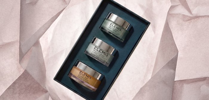 Trois pots de soin Elemis Pro-Collagen — crème de nuit, crème marine SPF 30, et baume nettoyant — dans une boîte cadeau noire sur un tissu pâle.
