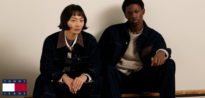 Chaqueta de denim con cuello marrón, combinada con una camisa a rayas. Suéter acogedor y pantalones oscuros. Dos modelos sentados, fondo neutro.