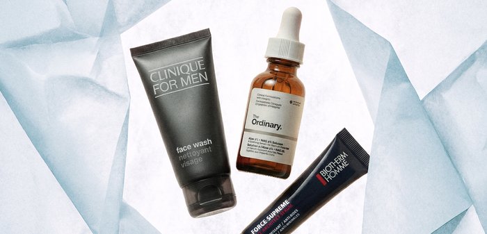 Trois produits de soins pour hommes : nettoyant visage Clinique, sérum The Ordinary avec compte-gouttes, et crème Biotherm Homme sur du papier blanc froissé.