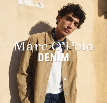 Młody mężczyzna w beżowej kurtce, białej koszuli i wzorzystym szalu stoi oparty o oświetloną słońcem beżową ścianę z napisem Marc O'Polo Denim.