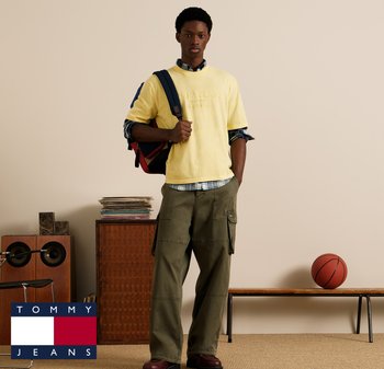 T-shirt en coton jaune avec logo en relief, porté sur une chemise à carreaux, associé à un pantalon cargo olive. Sac à dos et ballon de basket visibles.