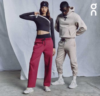 Due modelle posano con abbigliamento sportivo. Una indossa un top corto nero e pantaloni da jogging rossi. L'altra è vestita con una felpa con cappuccio beige e pantaloni da jogging coordinati.