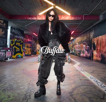 Zwarte nepbontjas, zwarte tanktop, oversized cargobroek in grijs met zakken, en chunky platformlaarzen, gezet tegen een graffiti-achtergrond.