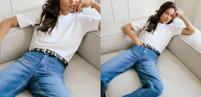 Vit bomullst-shirt kombinerad med blå jeans i denim, med ett svart bälte prytt med silvernitar. Modellen ligger avslappnat på en ljusgrå soffa.