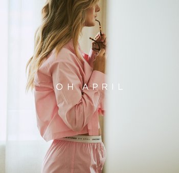 Rosa, kurze Bluse mit Knöpfen, kombiniert mit passender Hose, die einen Bund mit der Aufschrift "LOVE STORIES" hat. Das Haar ist wellig und lang.